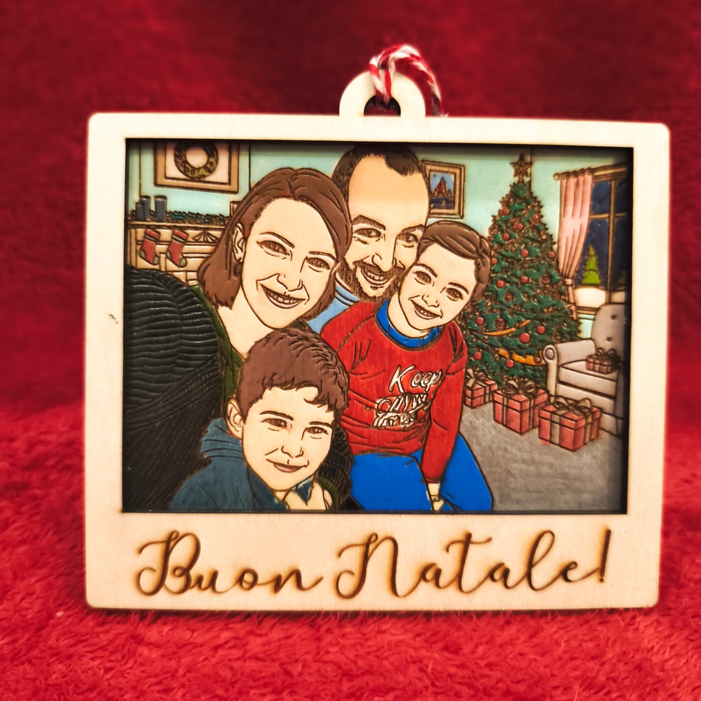 Ornamento natalizio in legno inciso con famiglia cartoon davanti all’albero di Natale e scritta “Buon Natale!”