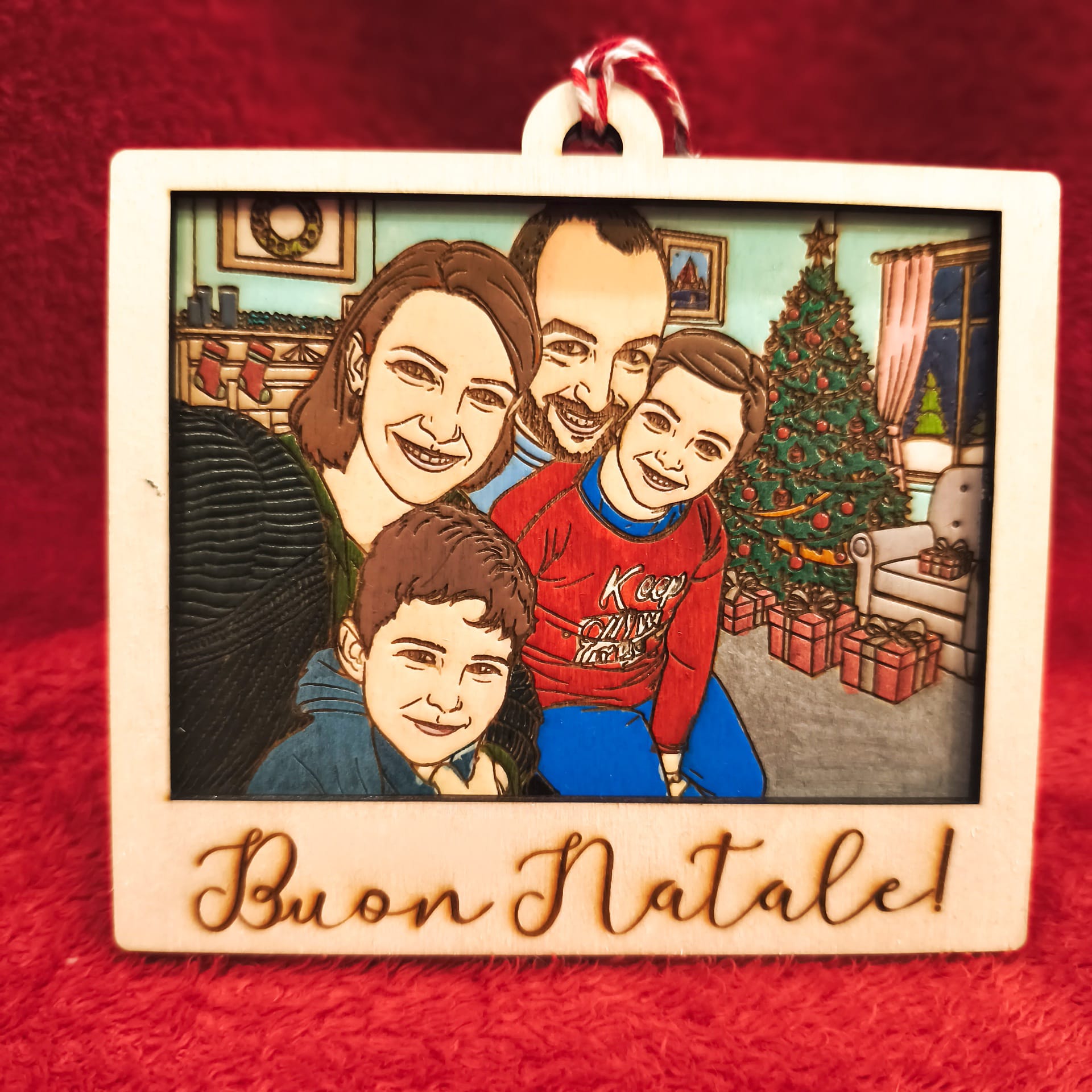 Ornamento natalizio in legno inciso con famiglia cartoon davanti all’albero di Natale e scritta “Buon Natale!”