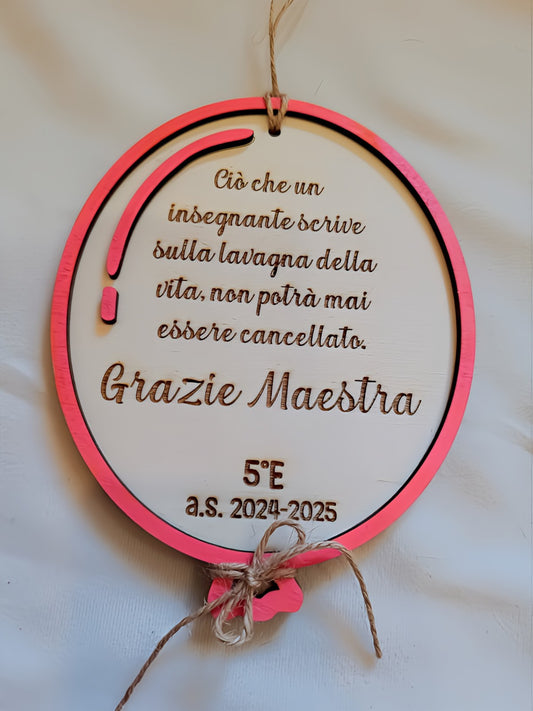 Targa rotonda in legno bianco con cornice multistrato fucsia-corallo, matita decorativa in legno rosa sul lato sinistro, incisione a pirografia della frase "Ciò che un insegnante scrive sulla lavagna della vita, non potrà mai essere cancellato. Grazie Maestra", personalizzazione 5°E a.s. 2024-2025, fiocco in cordino di iuta e cordino per appendere. Regalo di fine anno fatto a mano per insegnante.