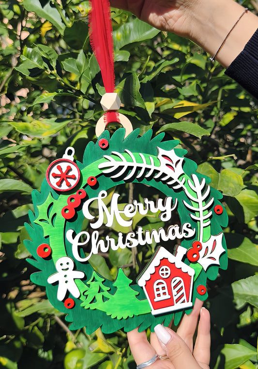 Hand holding Merry Christmas wreath ornament with red ribbon, gingerbread, and house outdoors