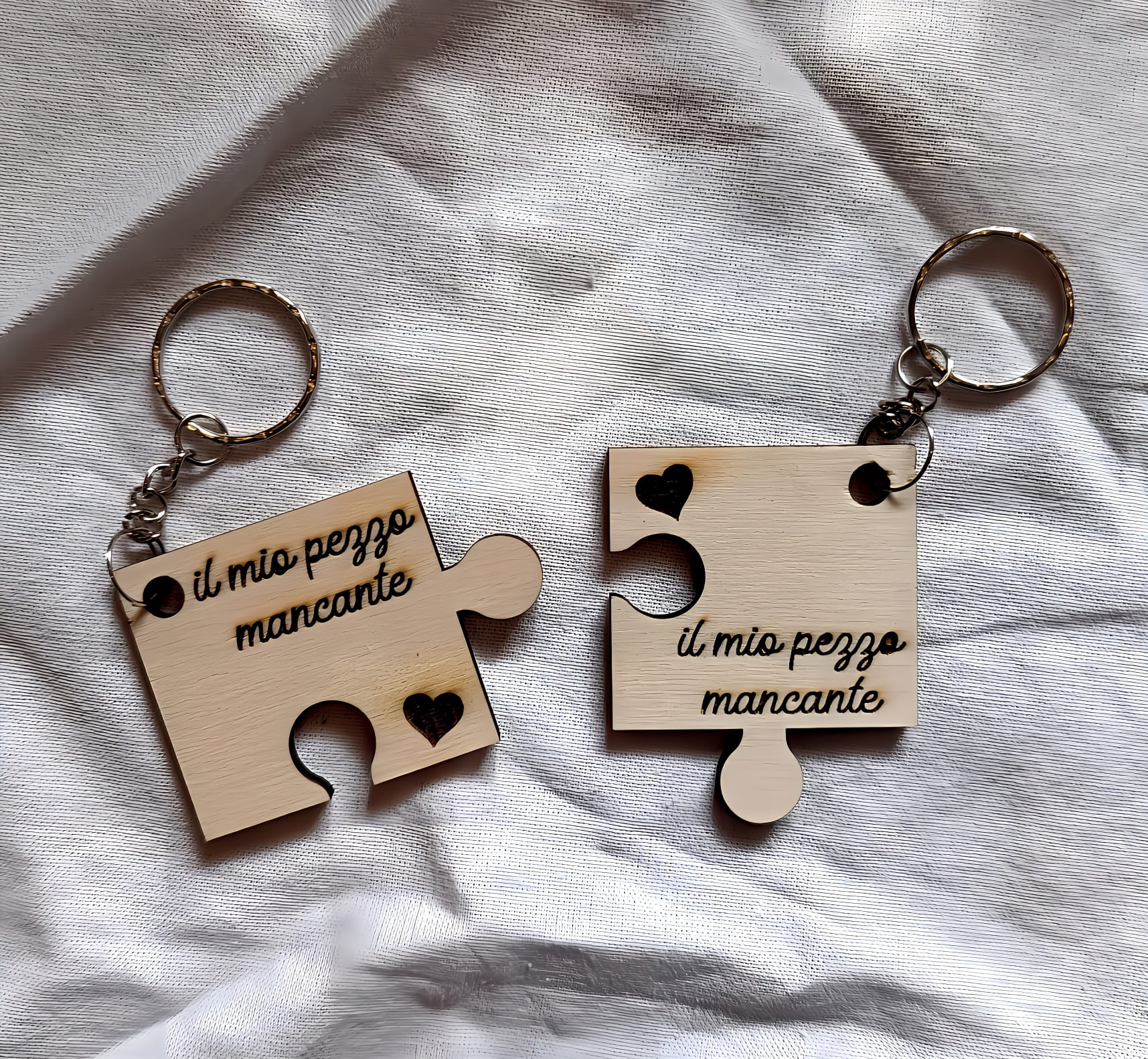 Wooden puzzle piece keychains with 'il mio pezzo mancante' on white fabric background