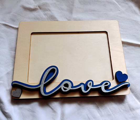 Wooden photo frame with blue love text and heart accents on a white fabric background