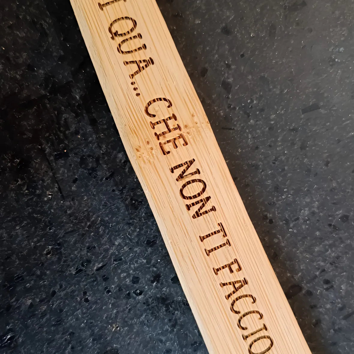 Bamboo kitchen utensil with Italian engraved text on dark stone countertop